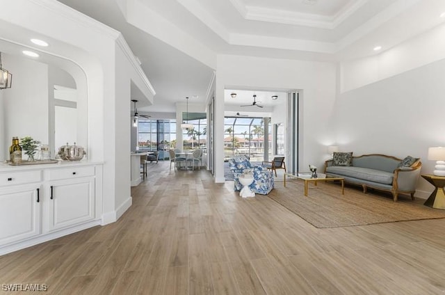 interior space with crown molding, light wood-type flooring, a raised ceiling, and ceiling fan