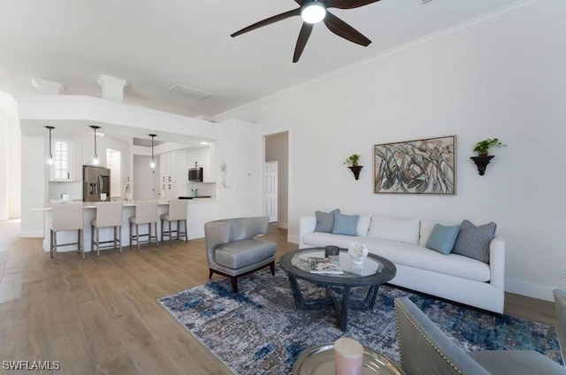 living room with light wood-style floors, ceiling fan, and crown molding