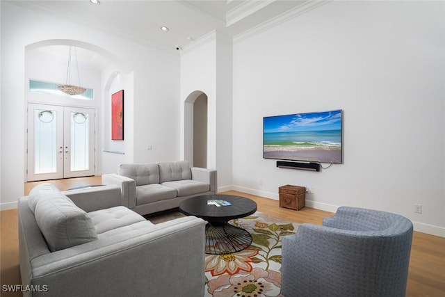 living area with arched walkways, french doors, crown molding, wood finished floors, and baseboards