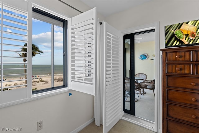 interior space with a view of the beach, light carpet, and a water view