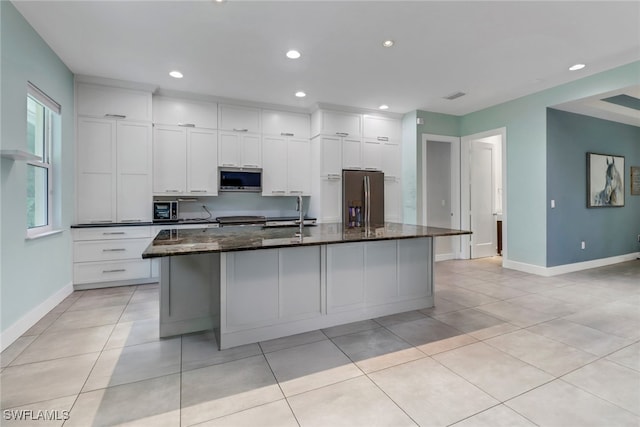 kitchen featuring dark stone counters, stainless steel appliances, a spacious island, sink, and white cabinetry