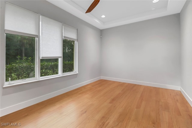 unfurnished room with a tray ceiling, ceiling fan, and light wood-type flooring