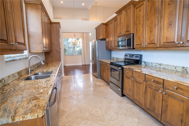 kitchen featuring stainless steel appliances, sink, decorative light fixtures, an inviting chandelier, and light stone counters