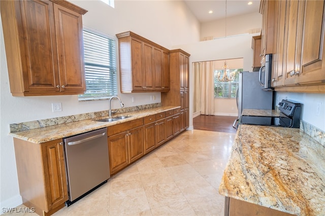 kitchen with light stone countertops, stainless steel appliances, an inviting chandelier, plenty of natural light, and sink