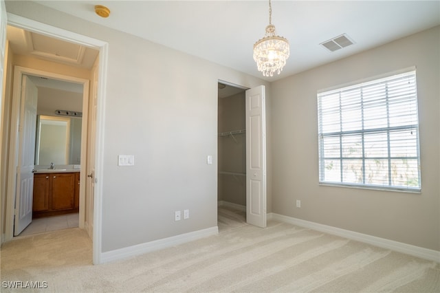 unfurnished bedroom with a spacious closet, a closet, an inviting chandelier, light carpet, and sink