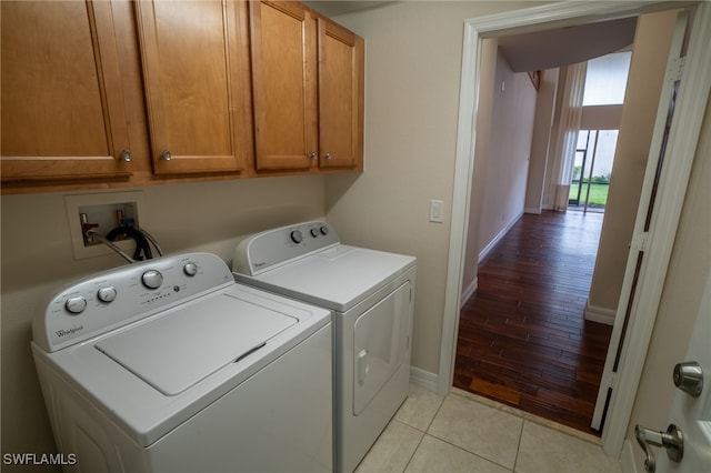 clothes washing area featuring cabinets, washing machine and clothes dryer, and light tile patterned floors