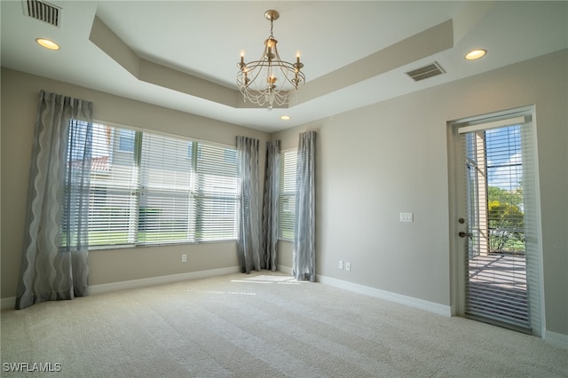 carpeted spare room with a healthy amount of sunlight, an inviting chandelier, and a tray ceiling