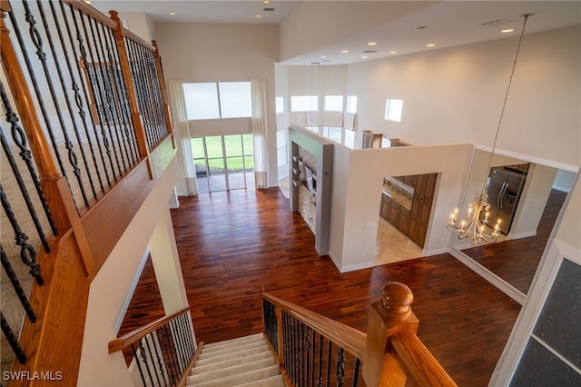 stairway with a towering ceiling, hardwood / wood-style flooring, and a notable chandelier