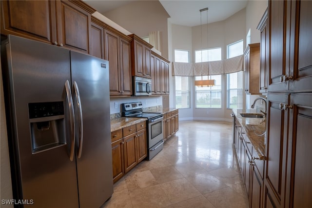 kitchen with a high ceiling, appliances with stainless steel finishes, light stone countertops, sink, and decorative light fixtures