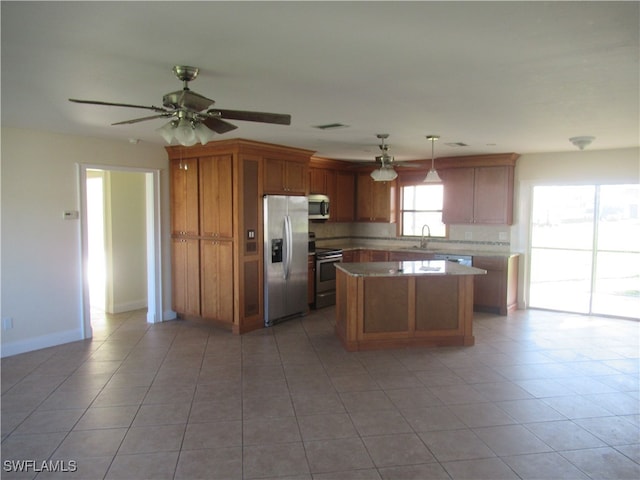 kitchen with light tile patterned floors, appliances with stainless steel finishes, sink, pendant lighting, and a center island