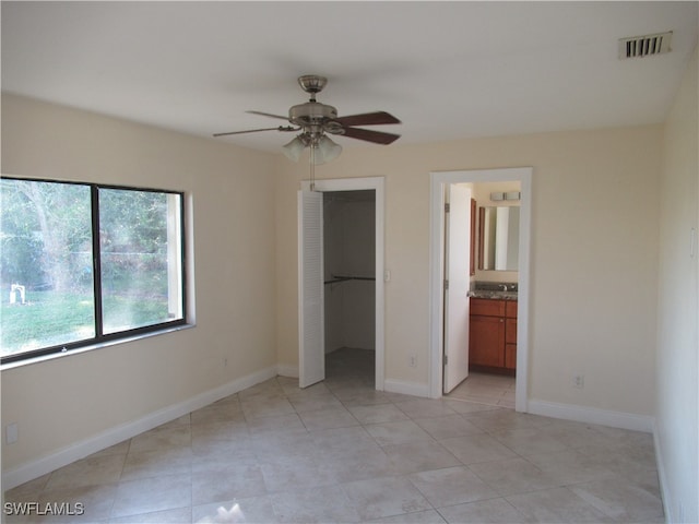 unfurnished bedroom with a closet, a spacious closet, light tile patterned floors, ensuite bathroom, and ceiling fan