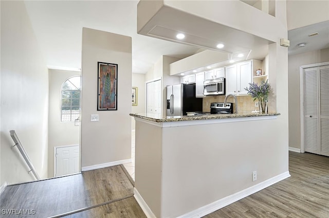 kitchen featuring stainless steel appliances, light stone countertops, white cabinets, kitchen peninsula, and light hardwood / wood-style flooring