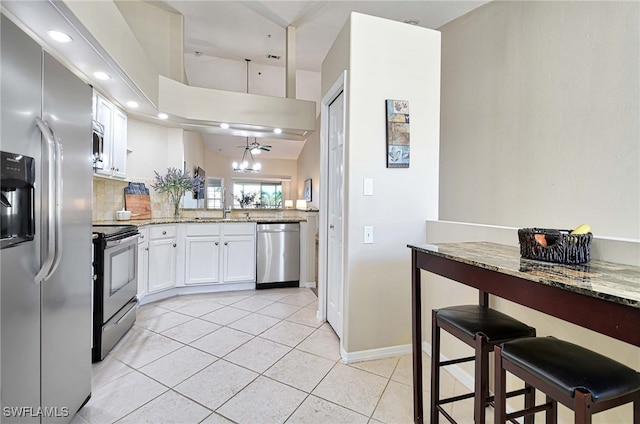 kitchen featuring white cabinetry, light stone counters, appliances with stainless steel finishes, light tile patterned floors, and lofted ceiling