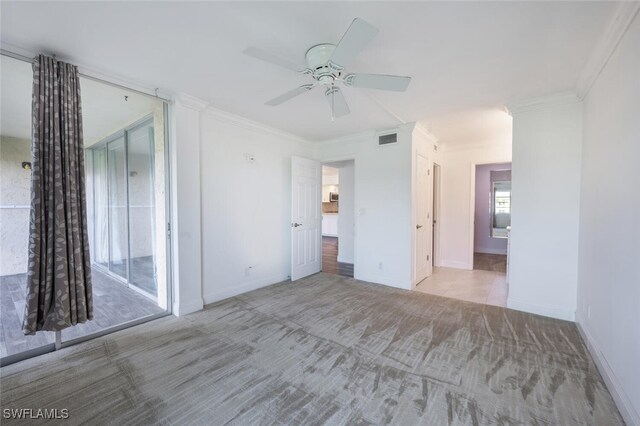 spare room with ceiling fan, crown molding, and light carpet