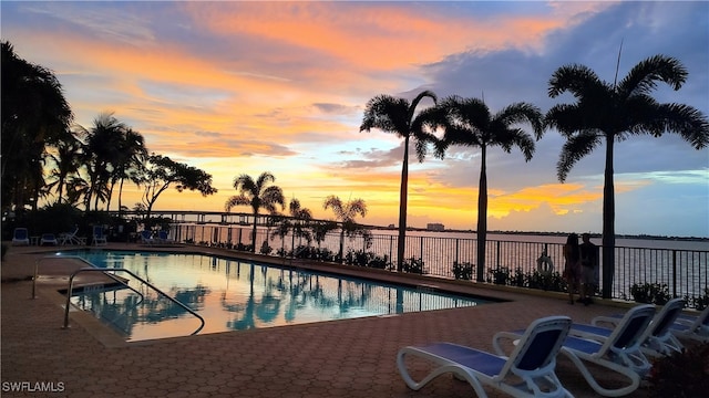 pool at dusk featuring a water view and a patio area