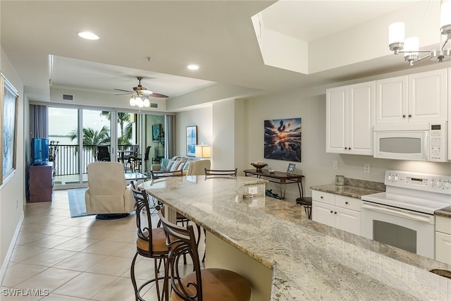 kitchen with white appliances, light stone countertops, hanging light fixtures, a kitchen breakfast bar, and white cabinets