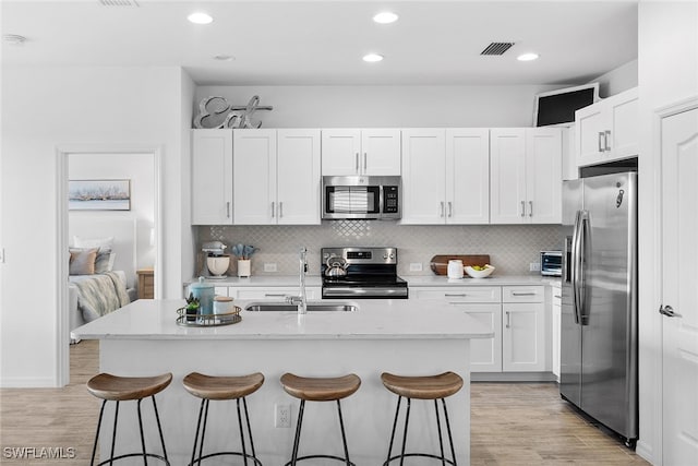 kitchen featuring light hardwood / wood-style flooring, sink, a kitchen bar, white cabinetry, and appliances with stainless steel finishes