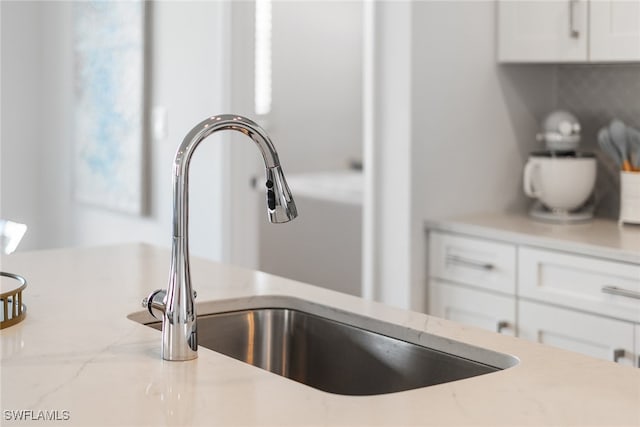 interior details featuring white cabinets, light stone countertops, and sink