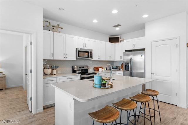 kitchen with light hardwood / wood-style floors, a kitchen island with sink, stainless steel appliances, and a kitchen bar