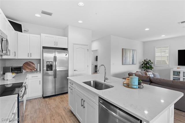 kitchen featuring a kitchen island with sink, sink, white cabinetry, appliances with stainless steel finishes, and light hardwood / wood-style floors