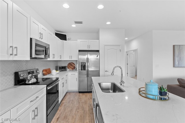 kitchen featuring white cabinets, light stone countertops, stainless steel appliances, and sink