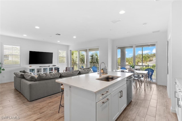 kitchen featuring dishwasher, a kitchen island with sink, sink, light wood-type flooring, and white cabinets