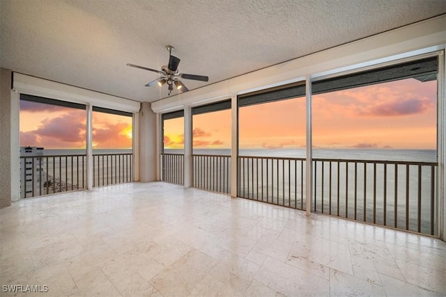 unfurnished sunroom featuring ceiling fan, a water view, and a beach view