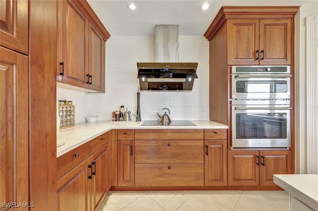 kitchen featuring light stone countertops, stainless steel double oven, wall chimney range hood, black electric stovetop, and light tile patterned floors