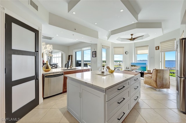 kitchen with ceiling fan, stainless steel appliances, light tile patterned floors, a raised ceiling, and white cabinets