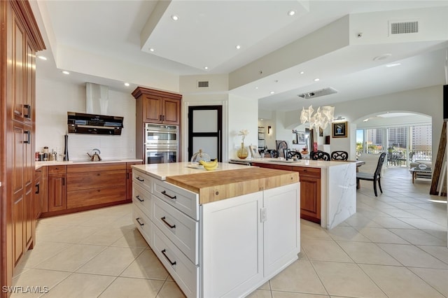 kitchen with white cabinets, a center island, light tile patterned floors, and butcher block countertops