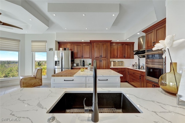 kitchen with light stone countertops, wall chimney exhaust hood, stainless steel appliances, sink, and white cabinetry