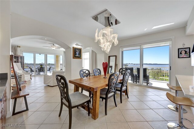 tiled dining room with ceiling fan with notable chandelier and a water view