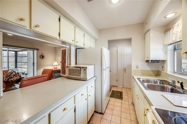 kitchen featuring sink, light tile patterned floors, stove, white cabinets, and a textured ceiling