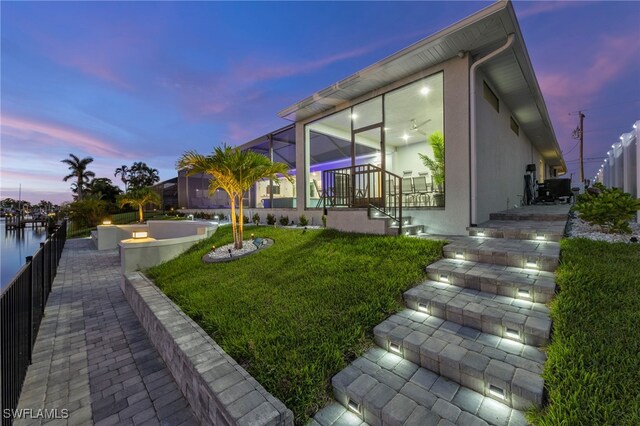 yard at dusk featuring glass enclosure and a water view