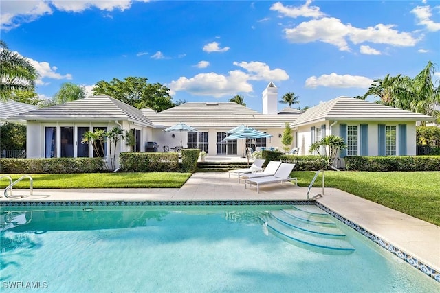 3323 Gin Ln, Naples, FL 34102 - rear view of property with an outdoor pool, a yard, a patio, a tiled roof, and a chimney