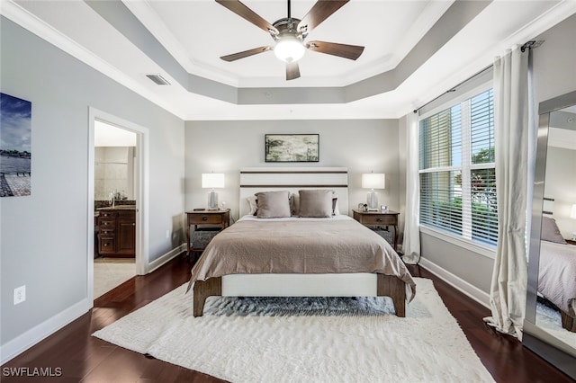 bedroom featuring ensuite bath, ceiling fan, a tray ceiling, crown molding, and dark wood-type flooring