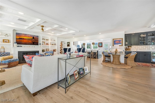 living room with beam ceiling, light hardwood / wood-style flooring, built in features, beverage cooler, and ceiling fan