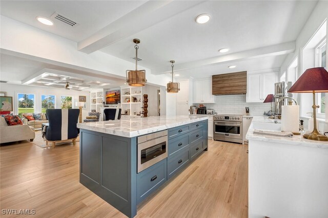 kitchen featuring white cabinets, beam ceiling, hanging light fixtures, appliances with stainless steel finishes, and light hardwood / wood-style flooring