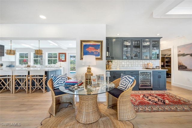 dining room with wine cooler, beam ceiling, bar, and light wood-type flooring