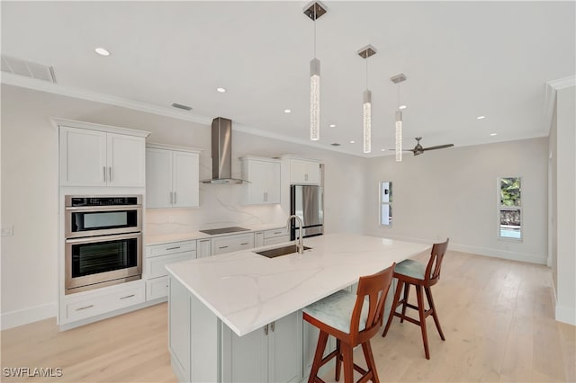 kitchen featuring sink, an island with sink, wall chimney exhaust hood, white cabinets, and light hardwood / wood-style flooring