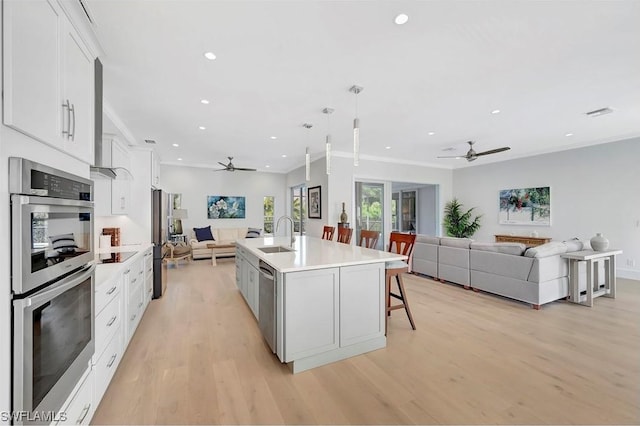 kitchen featuring sink, white cabinetry, stainless steel appliances, an island with sink, and decorative light fixtures