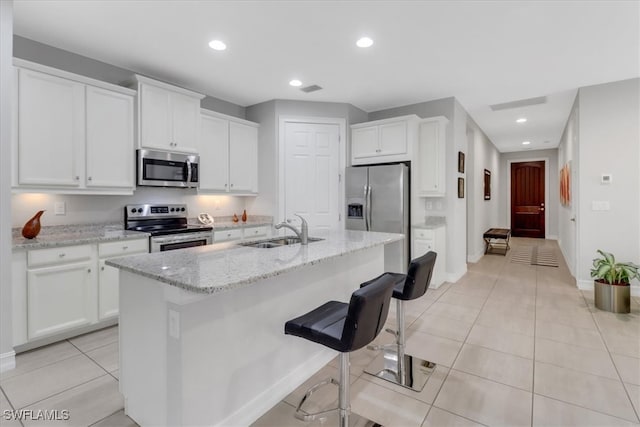 kitchen featuring sink, a kitchen island with sink, stainless steel appliances, light stone countertops, and white cabinets