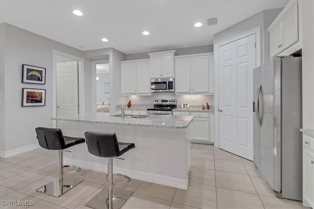 kitchen with an island with sink, white cabinets, light tile patterned floors, light stone counters, and stainless steel appliances