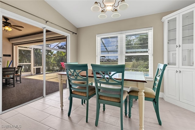 tiled dining area with a healthy amount of sunlight, ceiling fan with notable chandelier, and vaulted ceiling