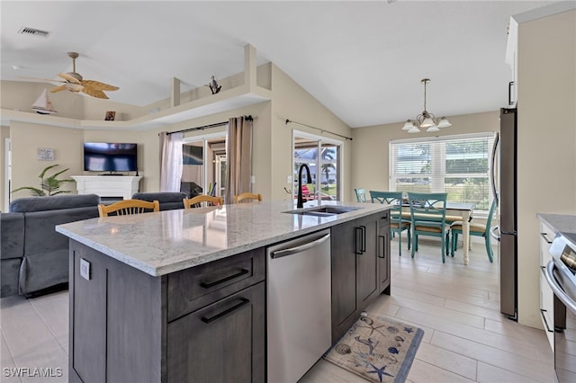 kitchen with light stone countertops, appliances with stainless steel finishes, sink, ceiling fan with notable chandelier, and a kitchen island with sink