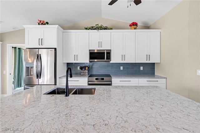 kitchen featuring light stone countertops, sink, white cabinetry, stainless steel appliances, and vaulted ceiling