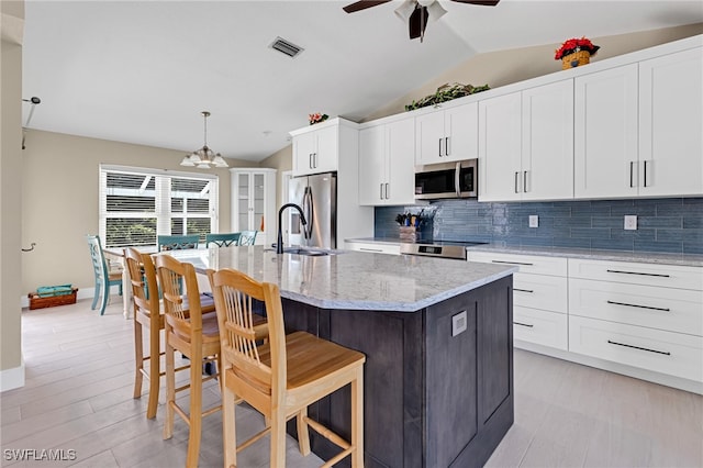 kitchen with a center island with sink, vaulted ceiling, appliances with stainless steel finishes, and hanging light fixtures