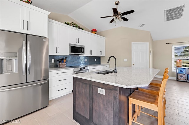 kitchen with appliances with stainless steel finishes, sink, vaulted ceiling, a breakfast bar area, and a center island with sink