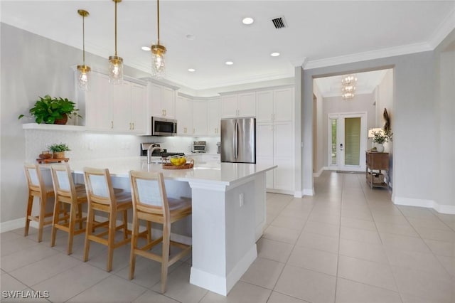 kitchen featuring white cabinets, appliances with stainless steel finishes, decorative light fixtures, light tile patterned floors, and a breakfast bar area