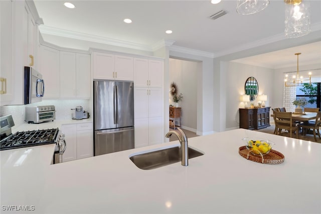 kitchen with pendant lighting, appliances with stainless steel finishes, white cabinetry, sink, and a notable chandelier